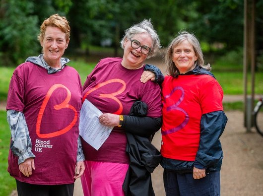 Three women wearing Blood Cancer UK t shirts smile at the camera.