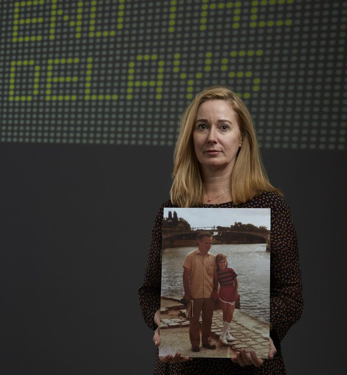 Diana Elkins stands holding a picture of her with her dad, who died of blood cancer.  Behind her on the wall it says end the delays.