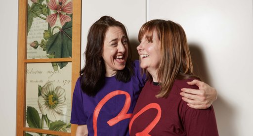 Two women in Blood Cancer UK t-shirts smile together, one has her arm around the other.