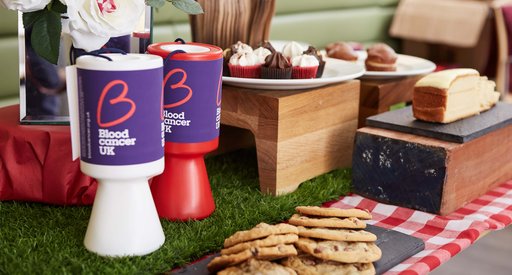 A table filled with delicious cakes and cookies, along with fundraising tins for a bake sale to raise money for Blood Cancer UK.