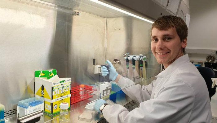 A scientists - Dr Christopher Kirkham - smiling at the camera while working in a lab