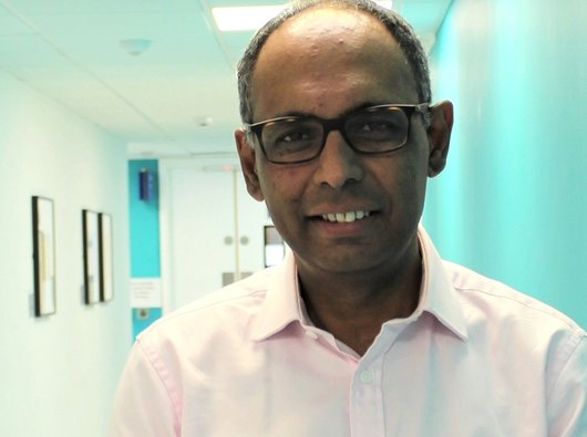 Portrait of Dr Rakesh Popat with a hospital corridor visible in the background.