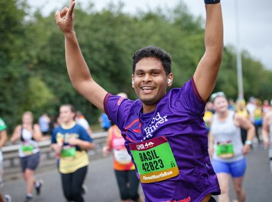 A male runner holds his arms up in the air making peace signs and smiling