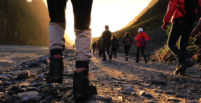 Low down photo of people walking away from the camera into the sunset in a rural location.