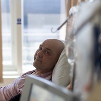 Image of a white man in bed in hospital. He is looking at the camera.