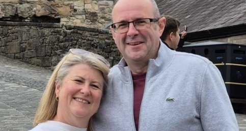 A couple stand together smiling at the camera.