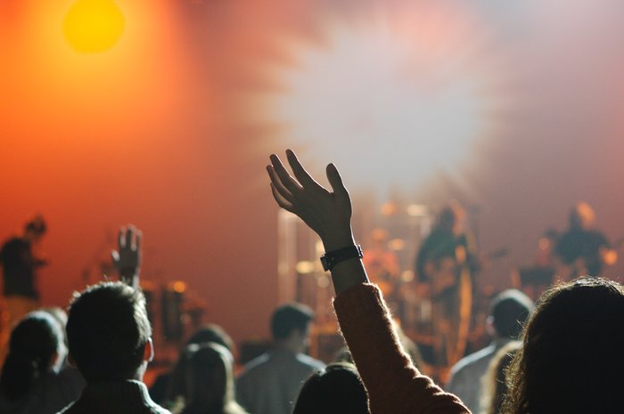 A stock image of a group of people with their hands in the air enjoying a blurred out band playing in the background.