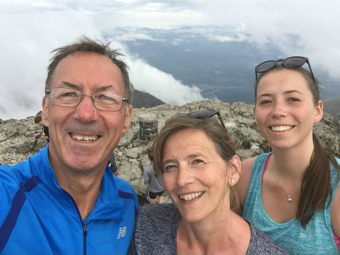Mel Plumridge and family, smiling with sunglasses atop their heads, with mountain in the background.