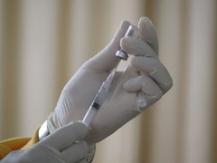 A hand wearing a surgical glove draws dose of vaccine into a hypodermic needle.