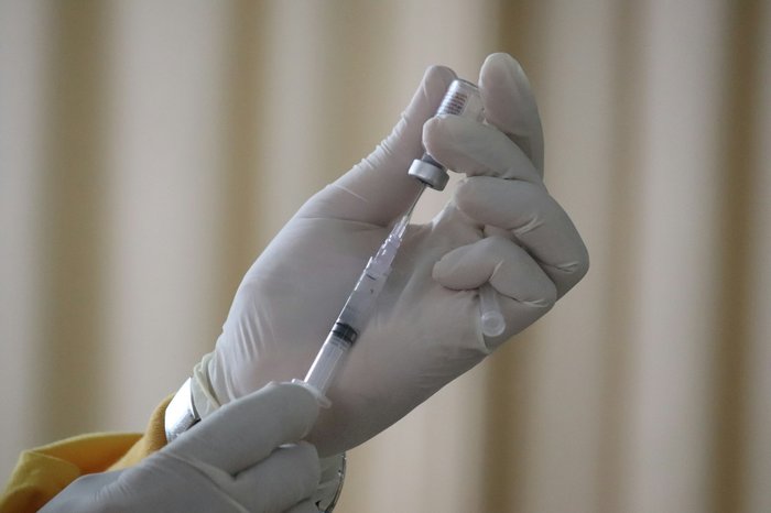 A hand wearing a surgical glove draws dose of vaccine into a hypodermic needle.