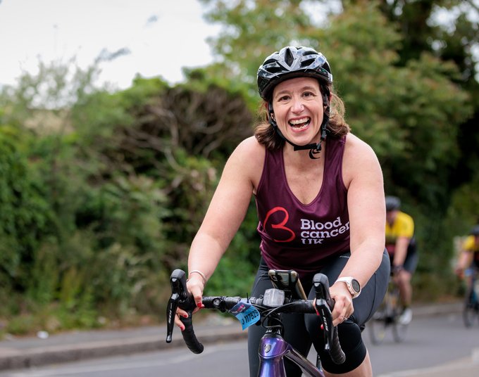 A woman smiles at the camera as she cycles through the countryside