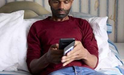 A man sitting on a bed, looking at his phone.