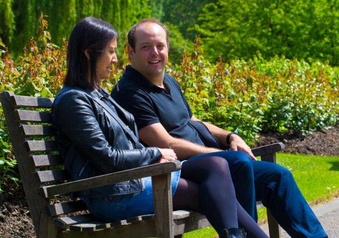 A man and woman share a friendly glance sat together on a park bench.