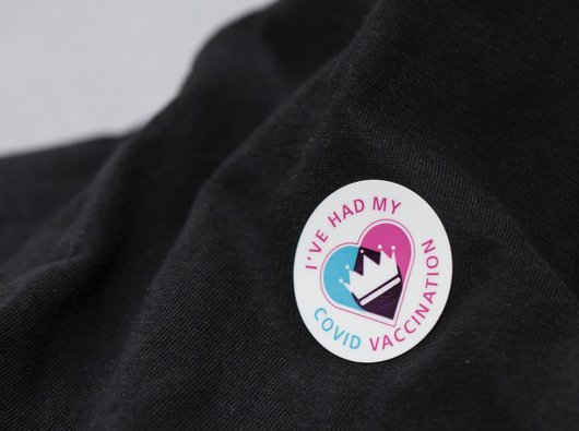 Close-up of a vaccination sticker showcasing that someone has had their Covid vaccine with a crown in the centre overlaying a heart.