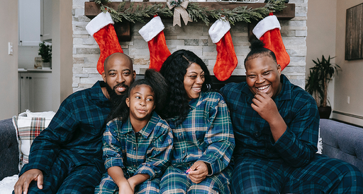 A family of four sitting on a sofa in pyjamas, with Christmas stockings behind them