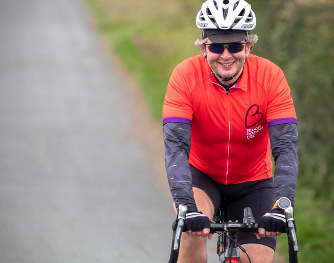 A cyclist heading down a country lane wearing a red Blood Cancer UK T shirt.