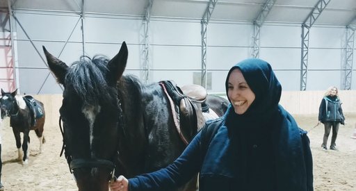 A woman (Federica) smiling in the direction of a horse, which she is stood next to.