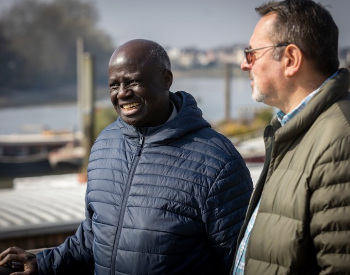 Two older male friends out walking by a river in a town.