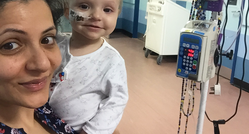 A mother and her very young child pose together in hospital surrounded by medical equipment.