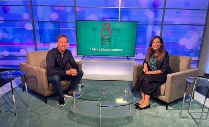 Two presenters sit in a TV studio smiling at the camera, a screen shows the Blood Cancer UK logo