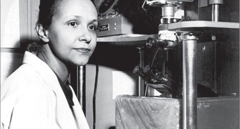 A scientist  - Jane C Wright, surgeon and early chemo researcher, poses next to a microscope in a black and white photograph.