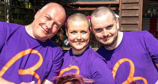 A woman - Jemma - shares a moment with two men. They all wear purple Blood Cancer UK T shirts.