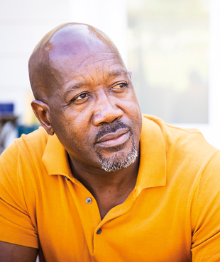 An older middle aged Black man in a yellow shirt.