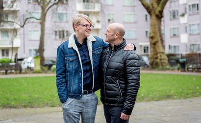 A male couple share a tender moment in a housing estate garden.