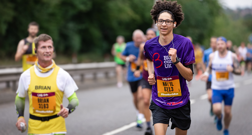 A woman running on a road wearing a purple blood cancer UK t shirt during a marathon.
