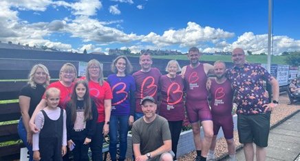 A large group of Blood Cancer UK supporters smile for the camera outside, under a blue sky dotted with clouds.