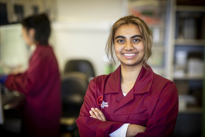 A researcher smiles at the camera, wearing a burgundy Blood Cancer UK lab coat