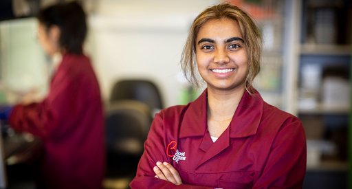 A researcher smiles at the camera, wearing a burgundy Blood Cancer UK jacket