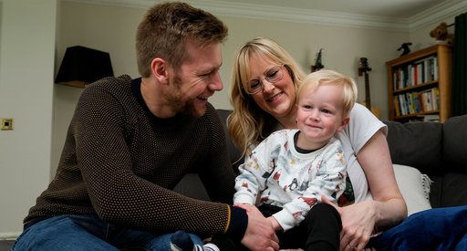 Emma and her partner sit on the sofa, holding and smiling at their baby son Tobias.