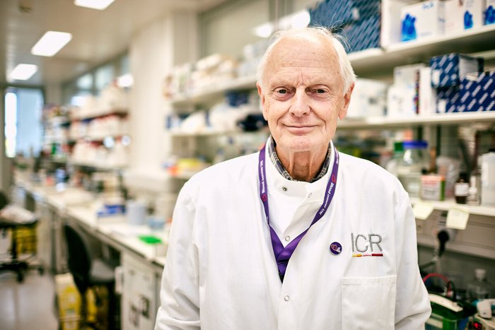 Professor Rabbitts stands in a lab, smiling at the camera