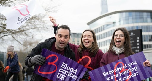 Three Blood Cancer UK staff all with cheery expressions, holding banners at a cheer point for one of our sports events.