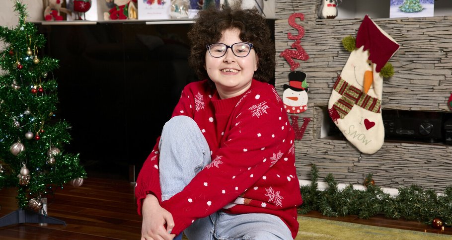 A picture of Alyssa, who is in remission from blood cancer, smiling in her Christmas jumper, surrounded by decorations.