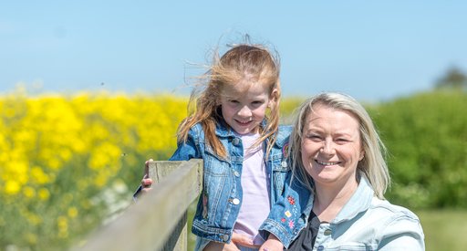 Mum and daughter smiling in sunny field with flowers.