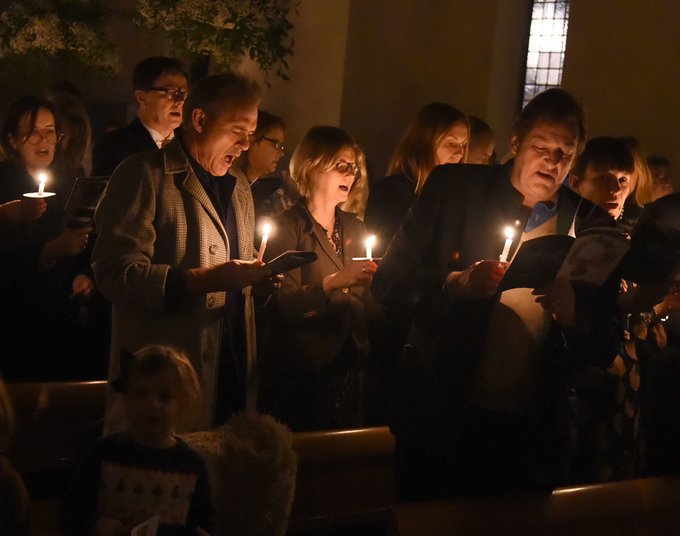 A group of people sing Christmas carols in a dark, candlelit room