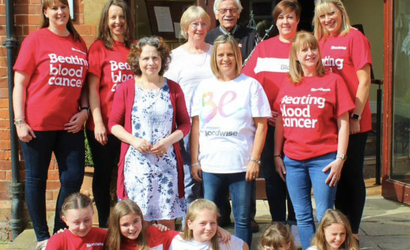 A group of women of various ages and generations - plus one man - poses together against a house in a backgarden.
