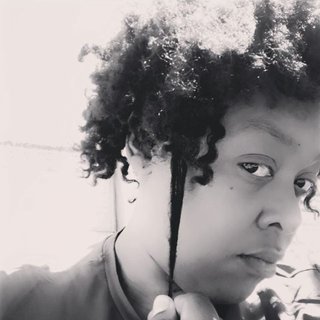 Black and white photograph of Simone, with medium length curly hair, looking serious and pulling at one curl.