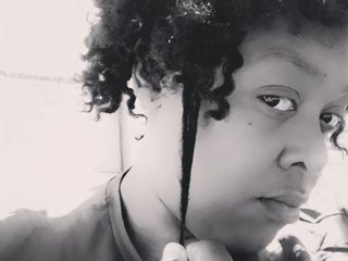 Black and white photograph of Simone, with medium length curly hair, looking serious and pulling at one curl.