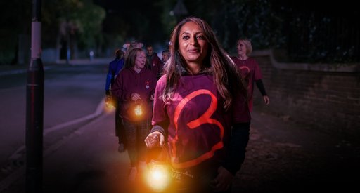 A woman wearing a Blood Cancer UK t-shirt leads a night time walk, holding a lantern, looking calm and happy.