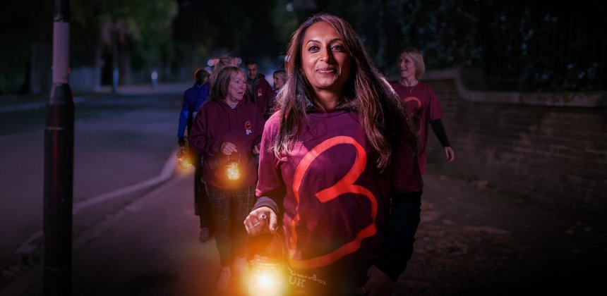 A woman wearing a Blood Cancer UK t-shirt leads a night time walk, holding a lantern, looking calm and happy.