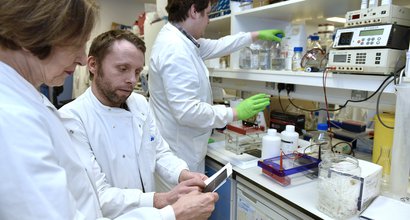 Three scientists check over some results on a report in a lab, surrounded by equipment.