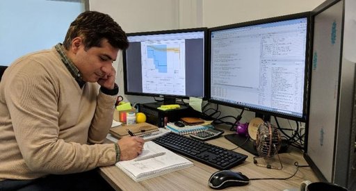 Dr Amir Enshaei writing on a note pad with three computer screens around him