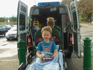 A child sits happy and beaming in a bed as he's loaded into an ambulence.
