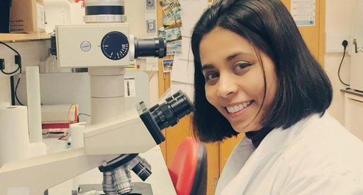 Anndita Roy - a researcher -  in a lab looking directly at the camera with a microscope
