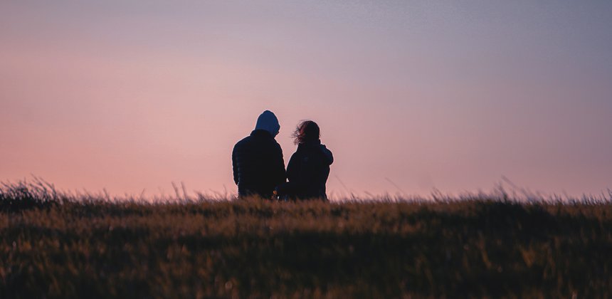 A couple out walking on a heath, seen from behind against the sky