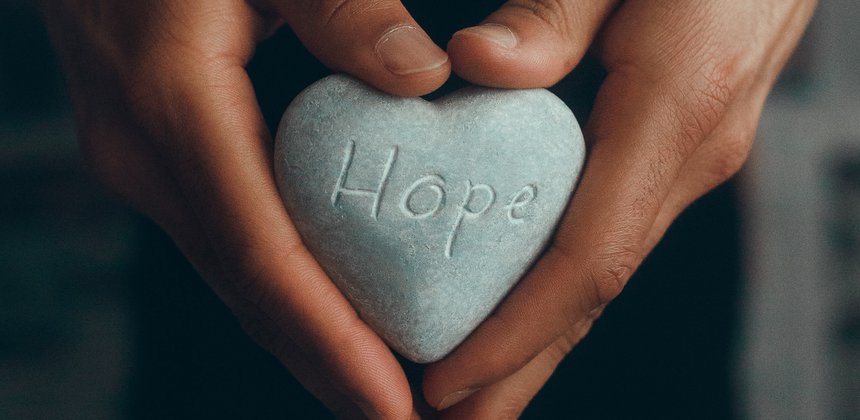 Image of hands holding a heart-shaped stone with the word "hope" carved on it.
