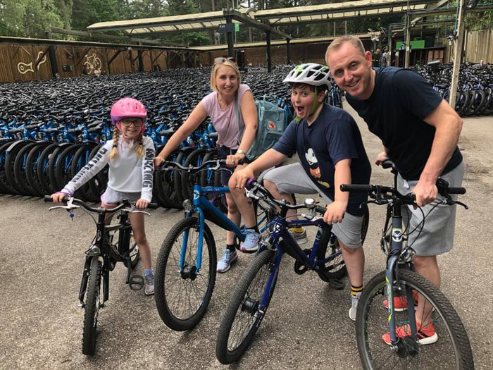 A family of cyclists - two parents, two children - pose for a photograph in front of a bikeshed.